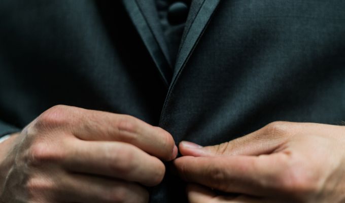 Zdjęcie przedstawia tors mężczyzny, który zapina guziki od marynarki garniturowej
