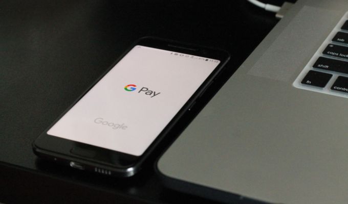 Zdjęcie przedstawia telefon z logo Google Pay na wyświetlaczu. Telefon leży obok laptopa.